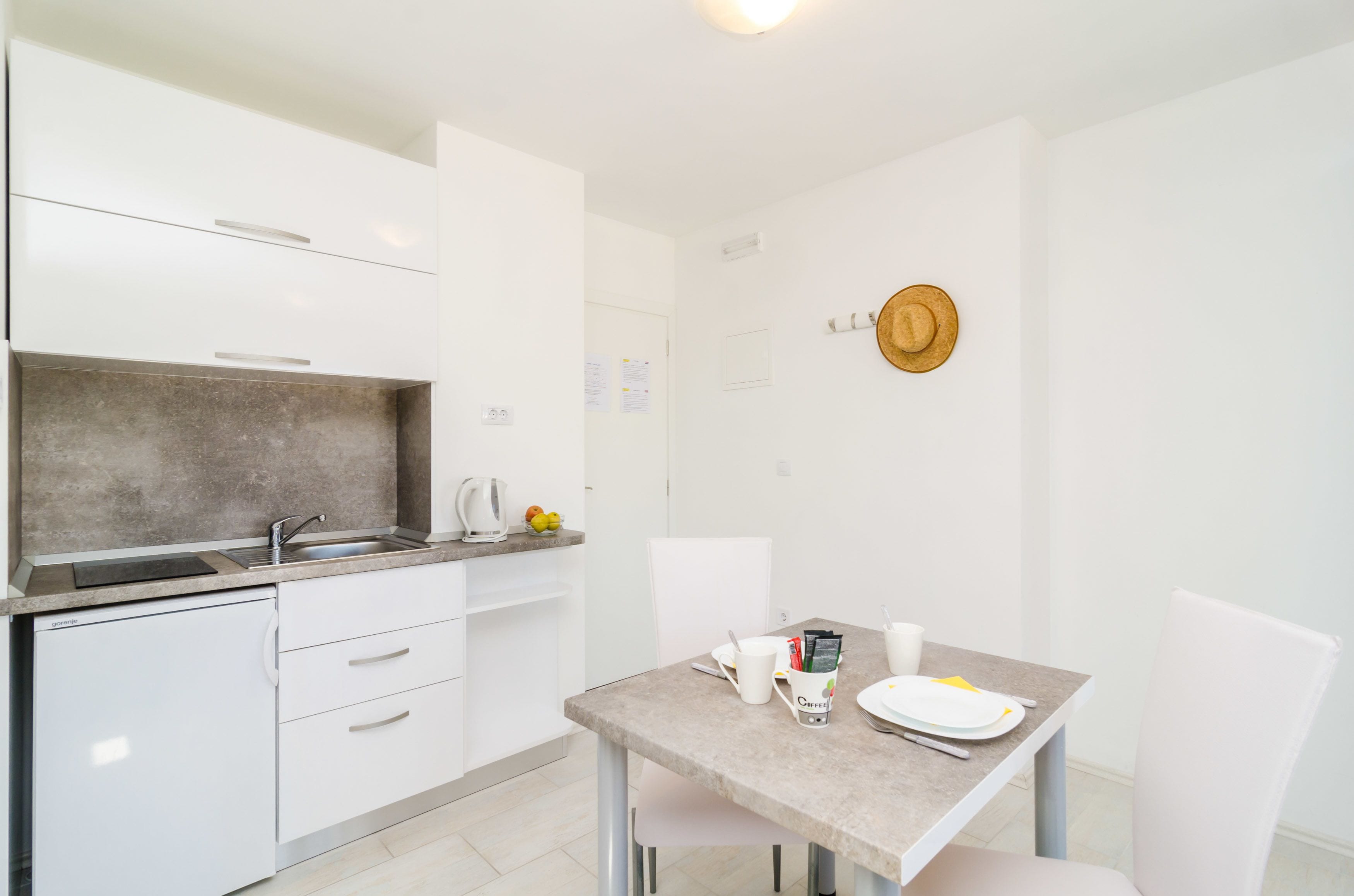 A compact kitchen with white cabinets, a countertop, and a dining area with a table set for two.