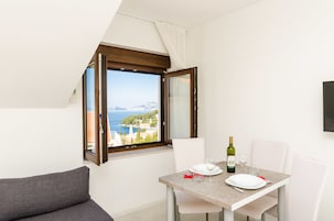 Zona pranzo con tavolo apparecchiato per due, vista sul mare e finestra con tende.