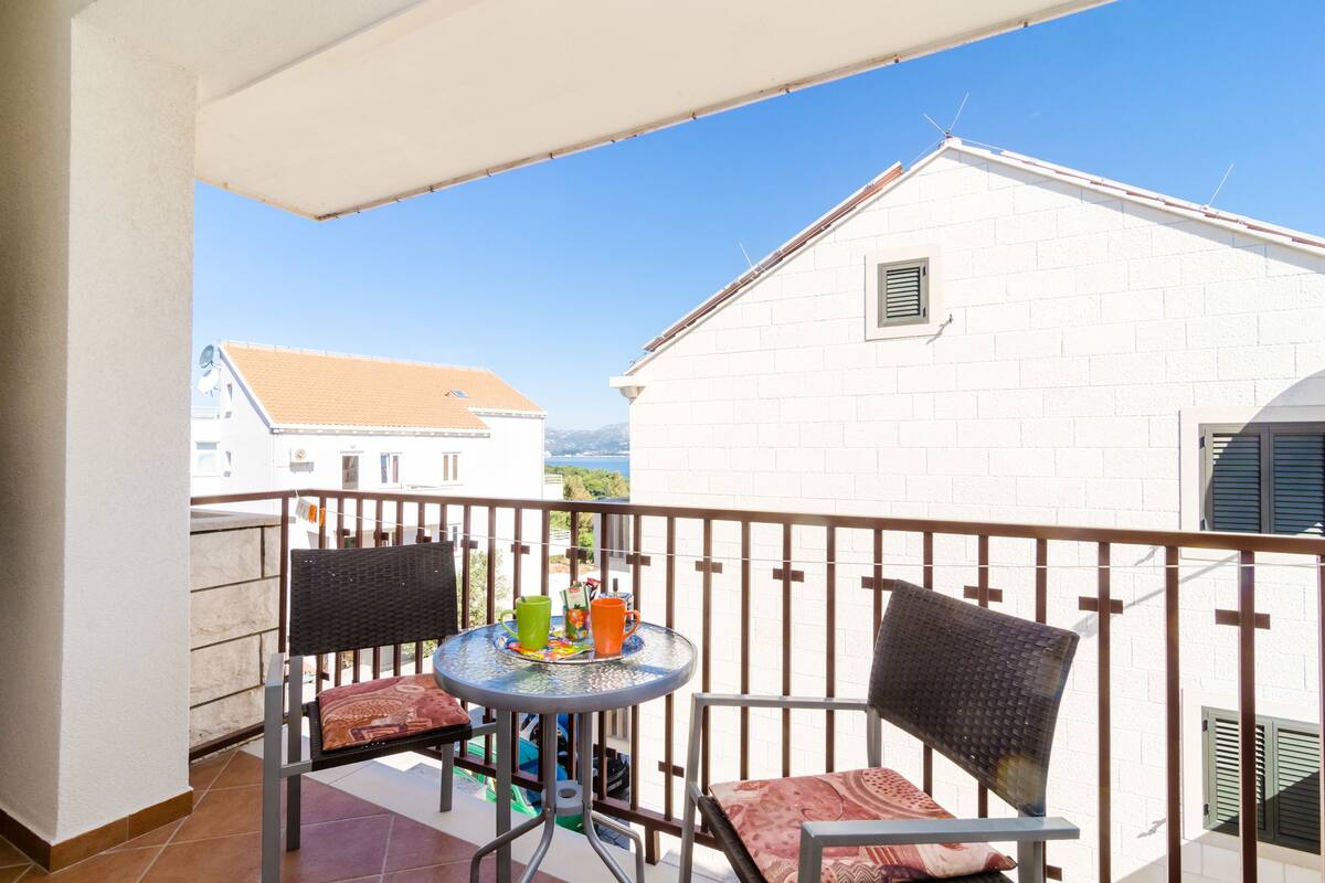 A balcony with a table and two chairs, a tiled floor, and a white building in the background.