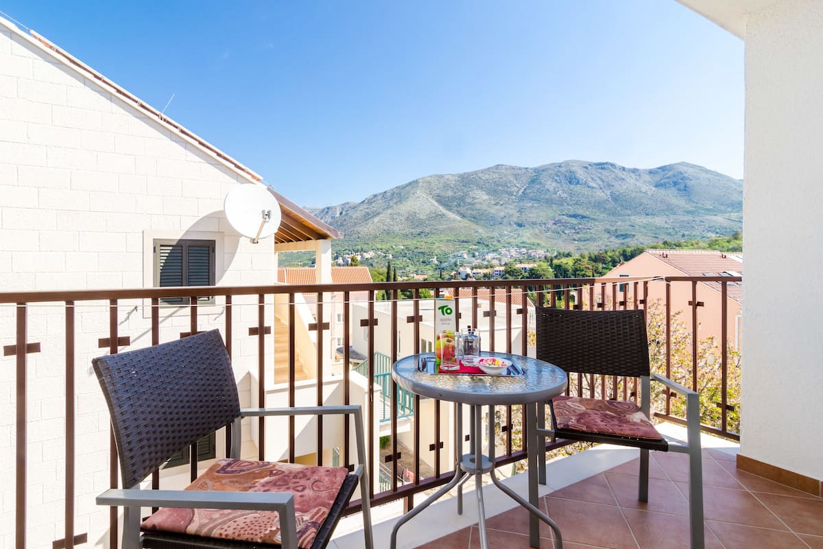 A balcony with two chairs and a table, overlooking a mountainous landscape.