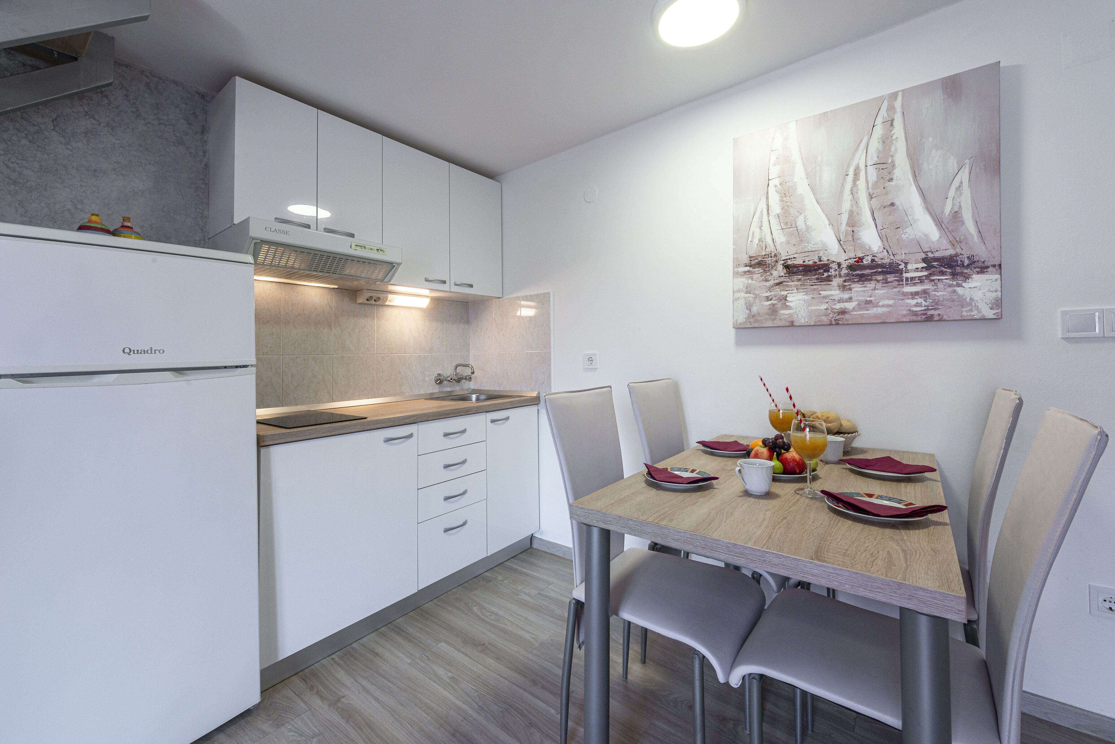 A modern kitchen with white cabinets, a built-in oven, and a dining area with a wooden table and chairs.