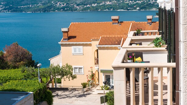 A coastal building with a tiled roof, a balcony with outdoor seating, and a view of the sea and mountains in the background. - Cina Apartments (Konavle)