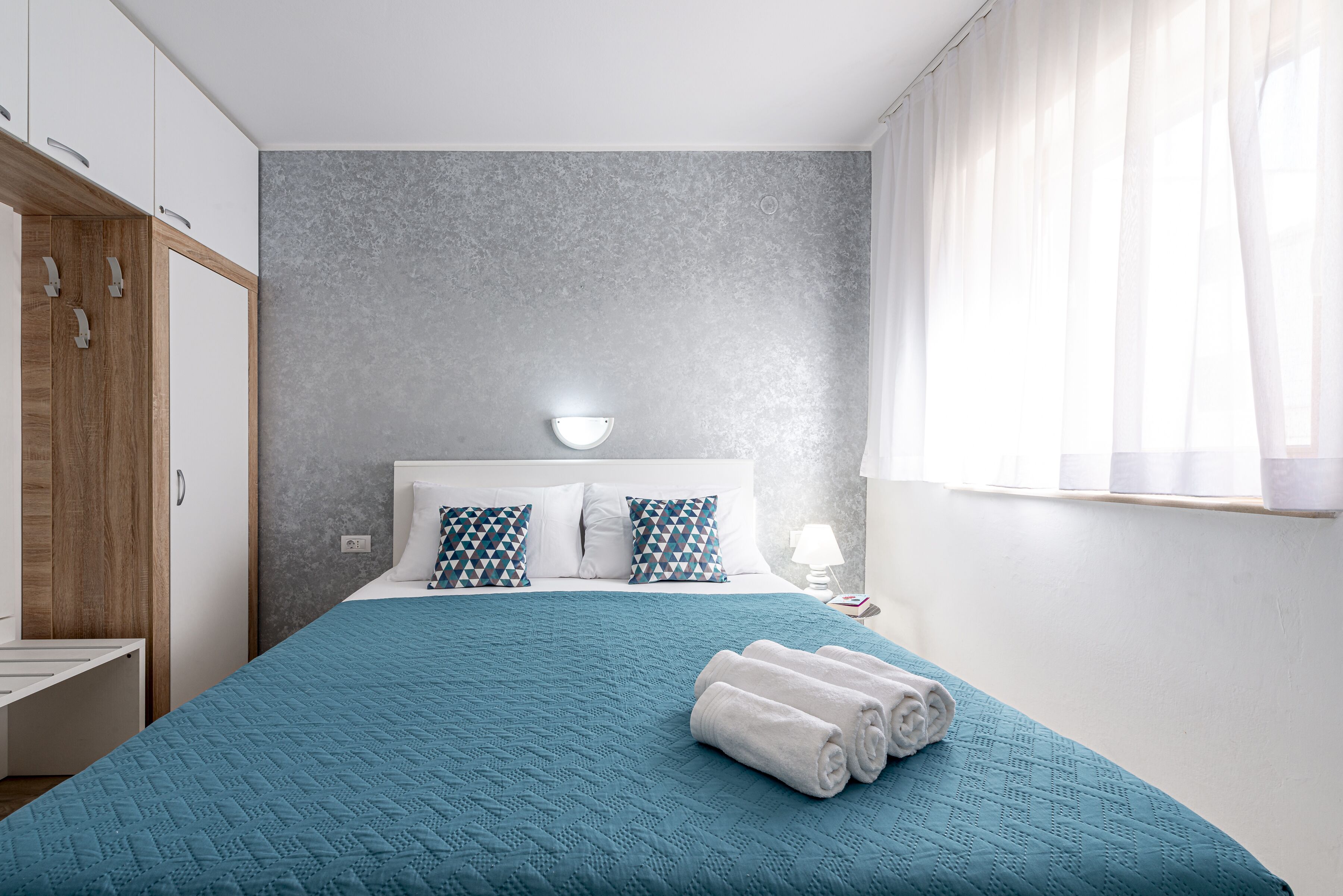 A bedroom with a bed, a nightstand, a lamp, and a window with curtains.