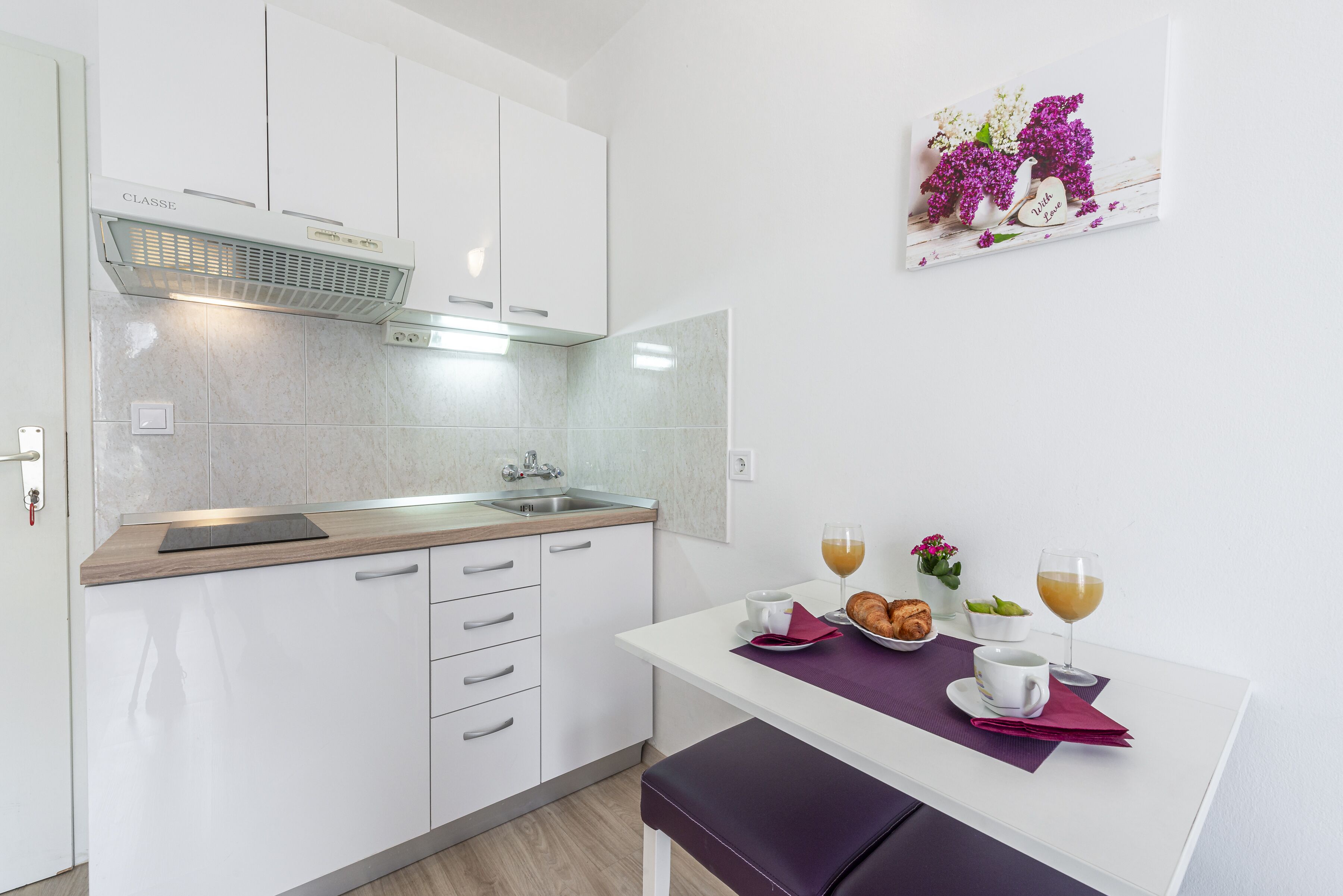 Una cucina moderna con mobili bianchi, un lavello in acciaio inossidabile e un'area pranzo con un tavolo apparecchiato per due.