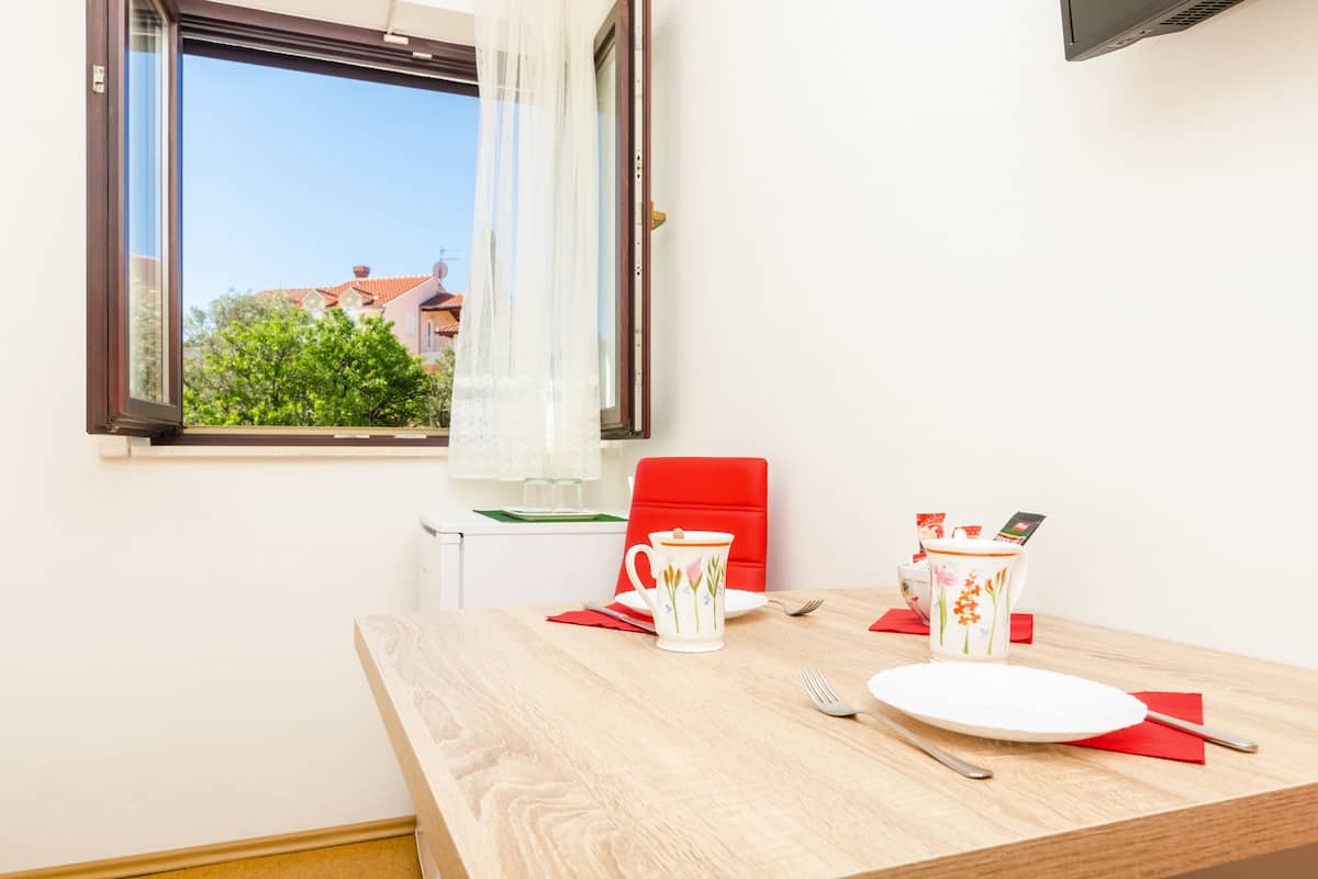 A dining area with a wooden table, red chair, and a window with a view of buildings and trees.