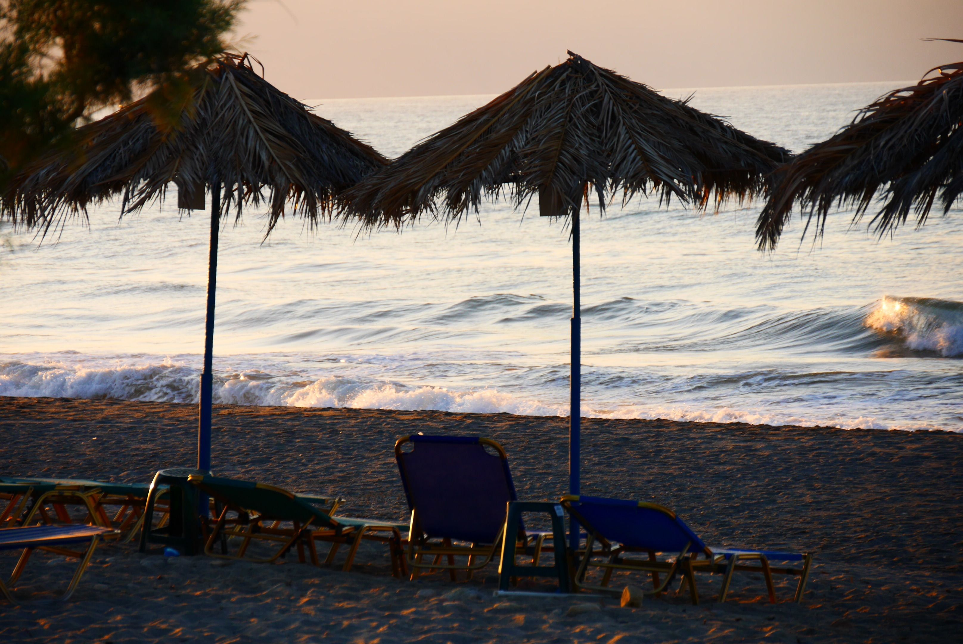 A beach with thatched umbrellas and wooden chairs facing the ocean.