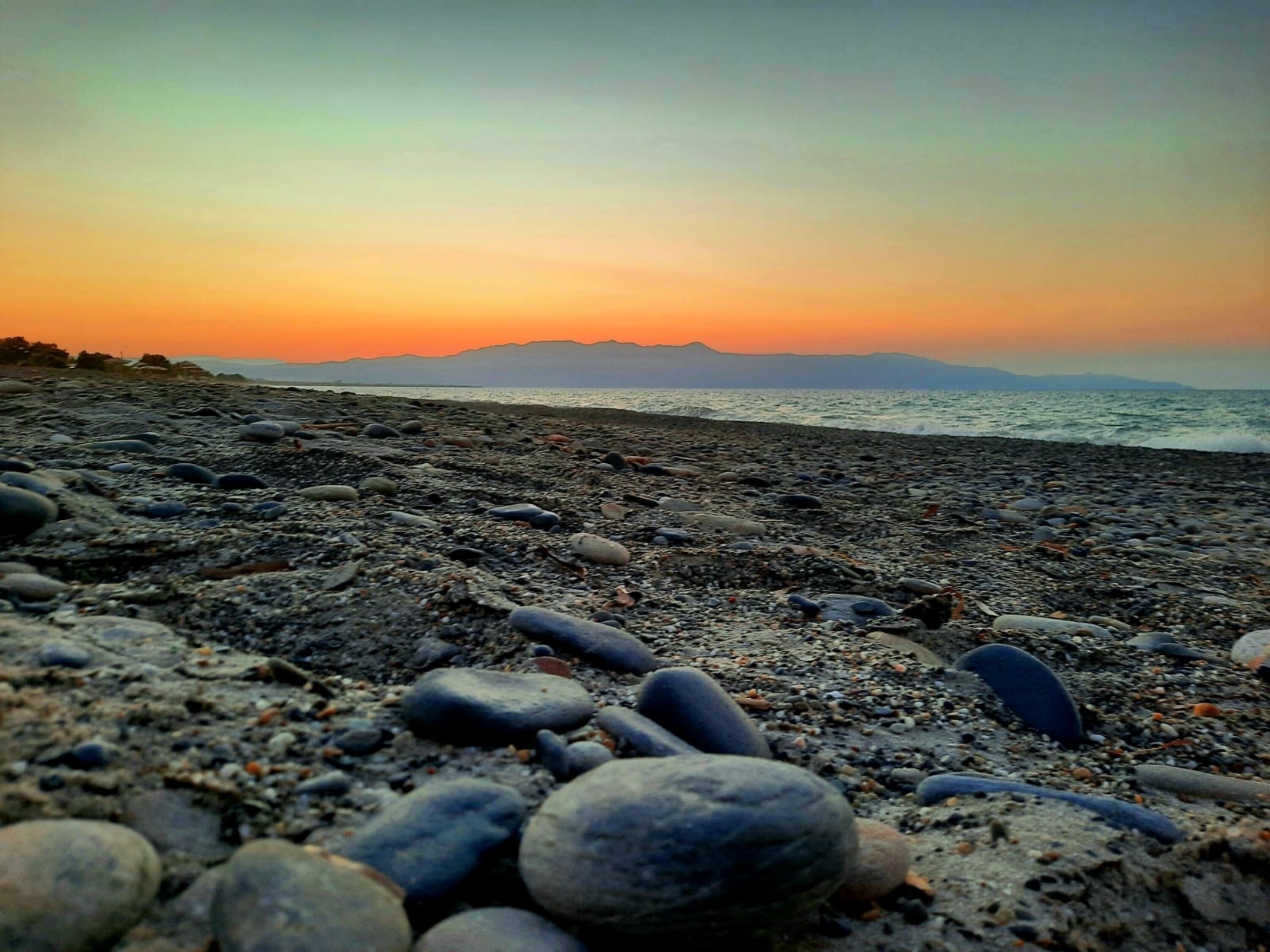 A pebbled beach with a sunset in the background.