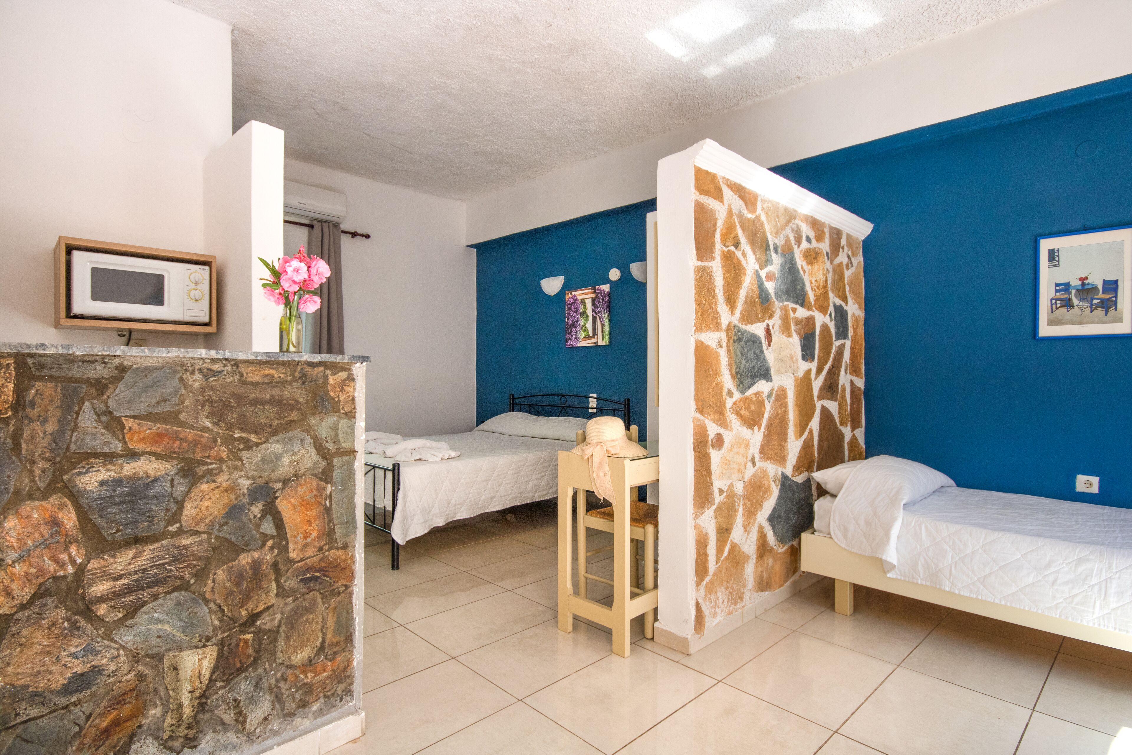 A room with two beds, a stone wall, a blue accent wall, a small desk, and a microwave.