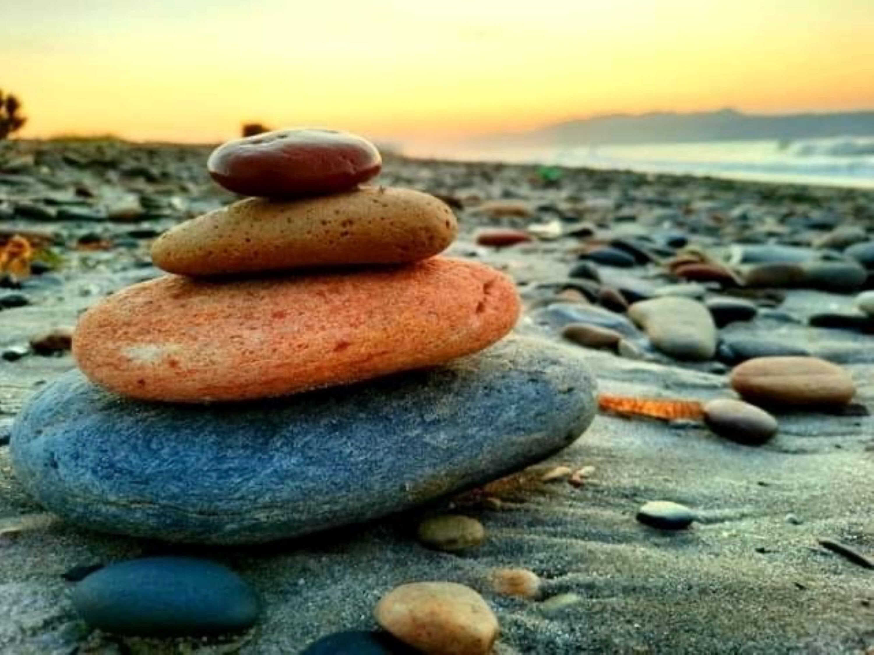 Un montón de piedras lisas sobre una playa arenosa con un atardecer de fondo.