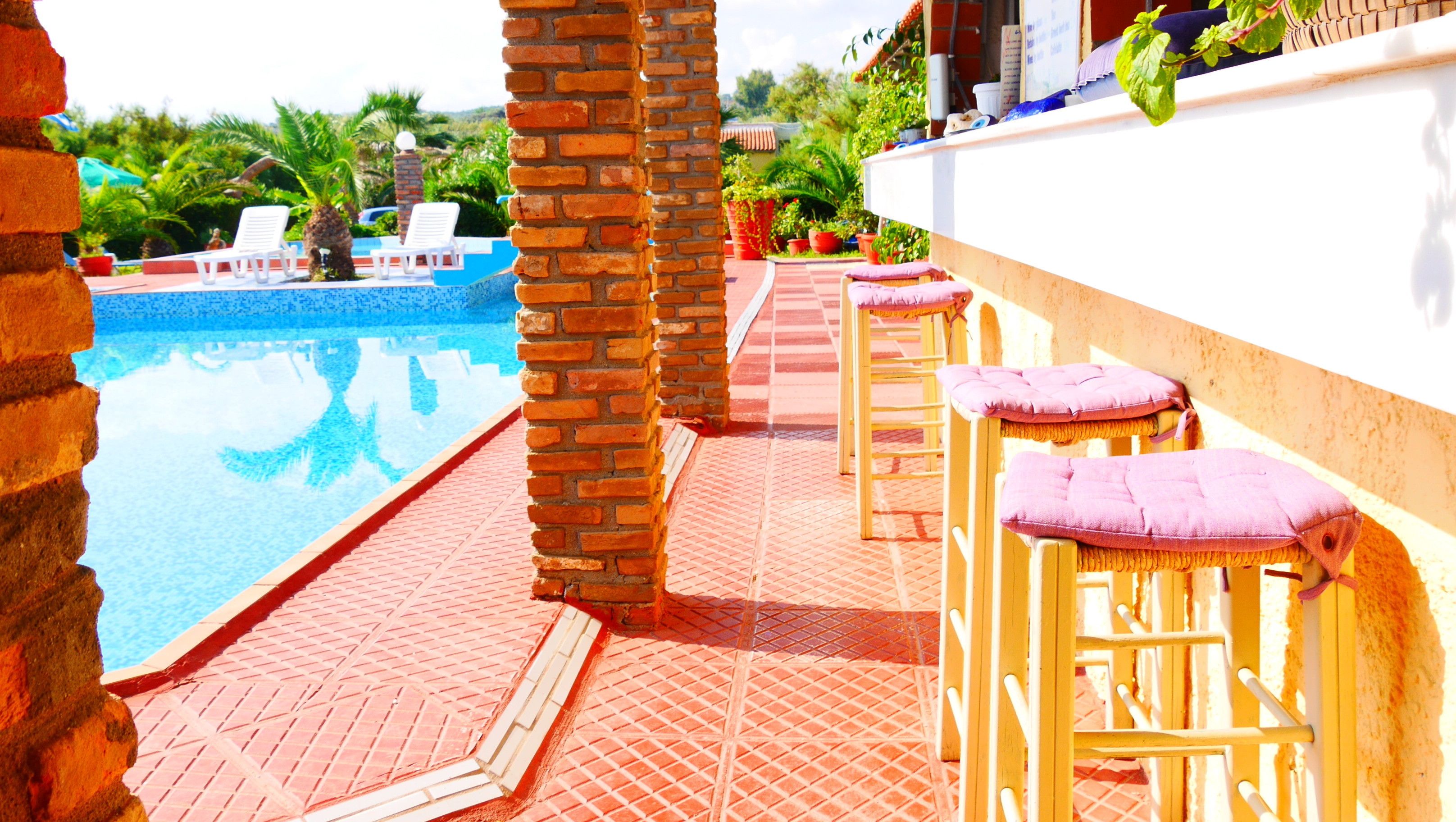 A poolside area with a brick wall, a pool, lounge chairs, and a bar with stools.