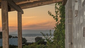 Un espace extérieur aménagé avec des murs en pierre, comprenant un banc en bois et une table, d’où l’on peut admirer un plan d’eau et un coucher de soleil.