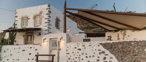 A white building with stone walls and a wooden staircase leading to the entrance.