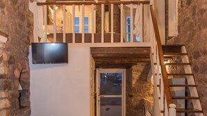 Un intérieur chaleureux avec un escalier en bois, un lustre, un téléviseur à écran plat et un mur en pierre.