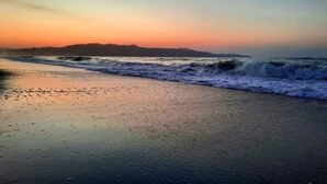 A beach at sunset with waves approaching the shore.