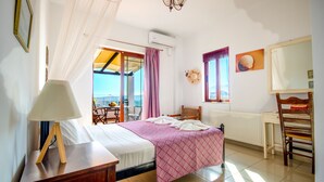 A bedroom with a bed, a desk, a chair, a lamp, a window with curtains, and a view of the outdoors.