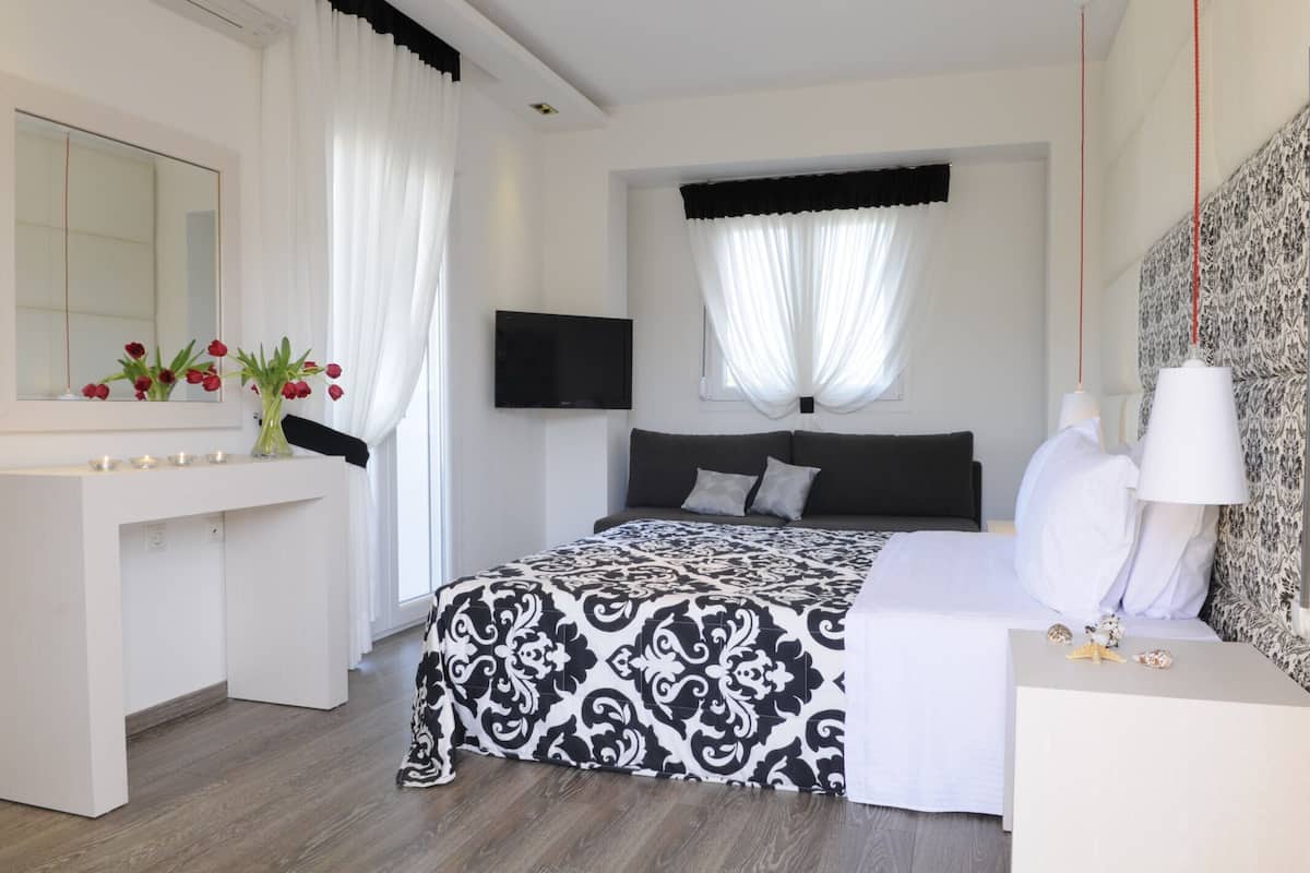 A modern bedroom with a large bed, a bedside table, a TV, and a mirror.