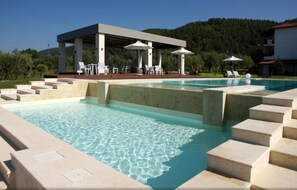 Una piscina amb aigua cristal·lina, escales per entrar-hi i una zona d'estar coberta amb ombrelles.
