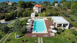 Vue aérienne d’un complexe hôtelier doté d’une piscine, de chaises longues et d’un patio couvert.