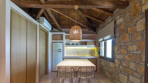 Une cuisine avec un mur en pierre, des poutres en bois au plafond, un luminaire suspendu et un réfrigérateur.