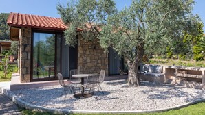 Un bâtiment en pierre avec un toit en tuiles, une porte vitrée et un patio comprenant une table et des chaises.