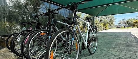 Bicycles parked under a green canopy on a paved area.
