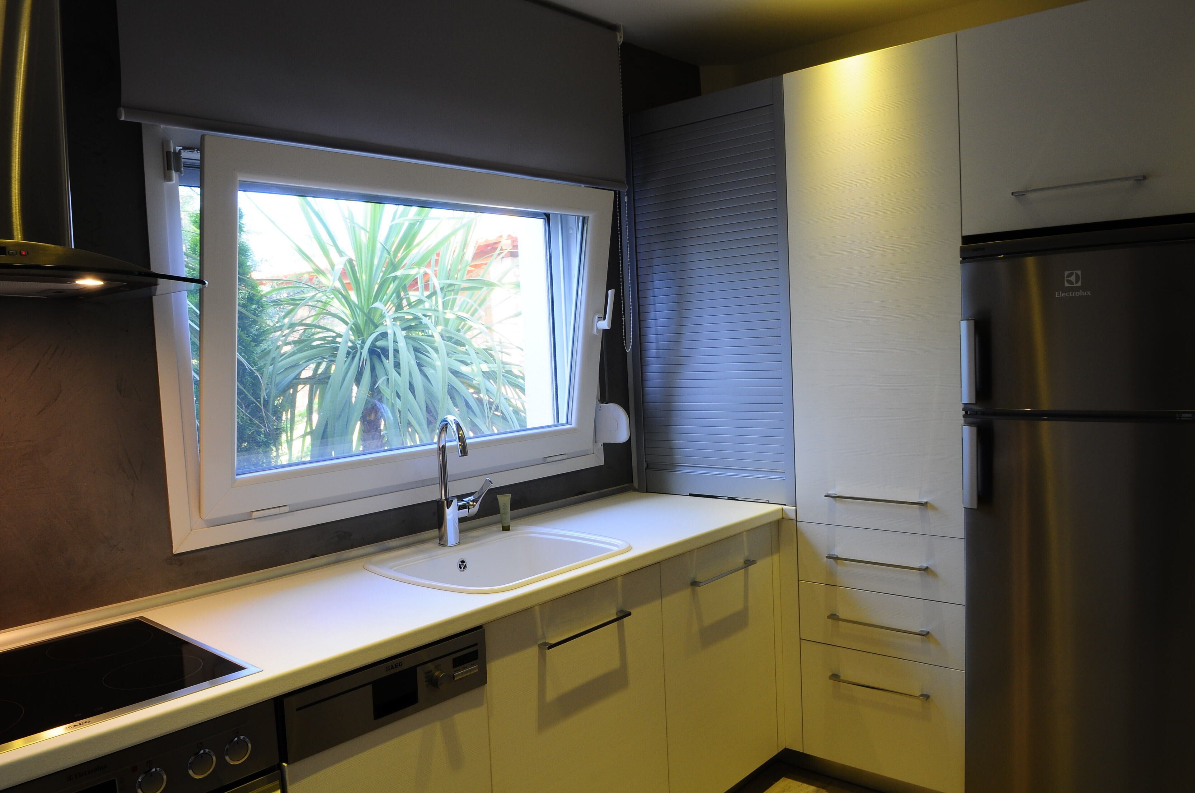 Una cocina con ventana, pileta, estufa y refrigerador.