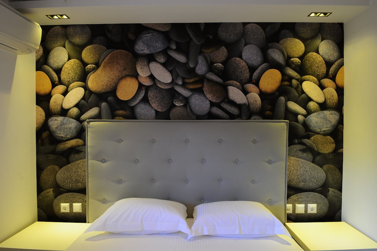 A bedroom with a headboard, two pillows, and a wall decorated with a variety of stones.