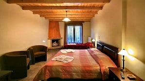 A cozy hotel room with a wooden ceiling, a fireplace, a bed with a red blanket, and a sitting area with chairs. - Guesthouse Teloni (Gortynia)