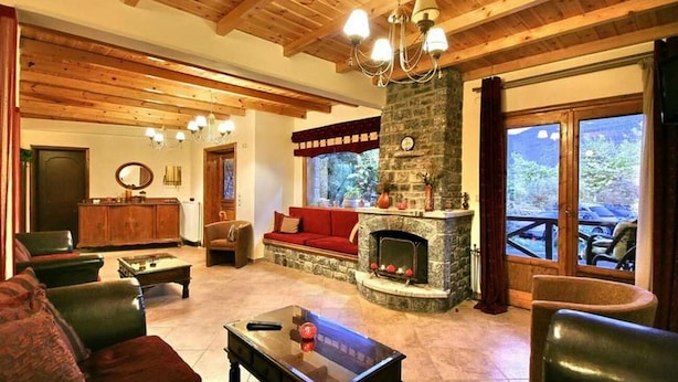 A cozy living room with a fireplace, wooden ceiling beams, and a view of the outdoors. - Guesthouse Teloni (Gortynia)