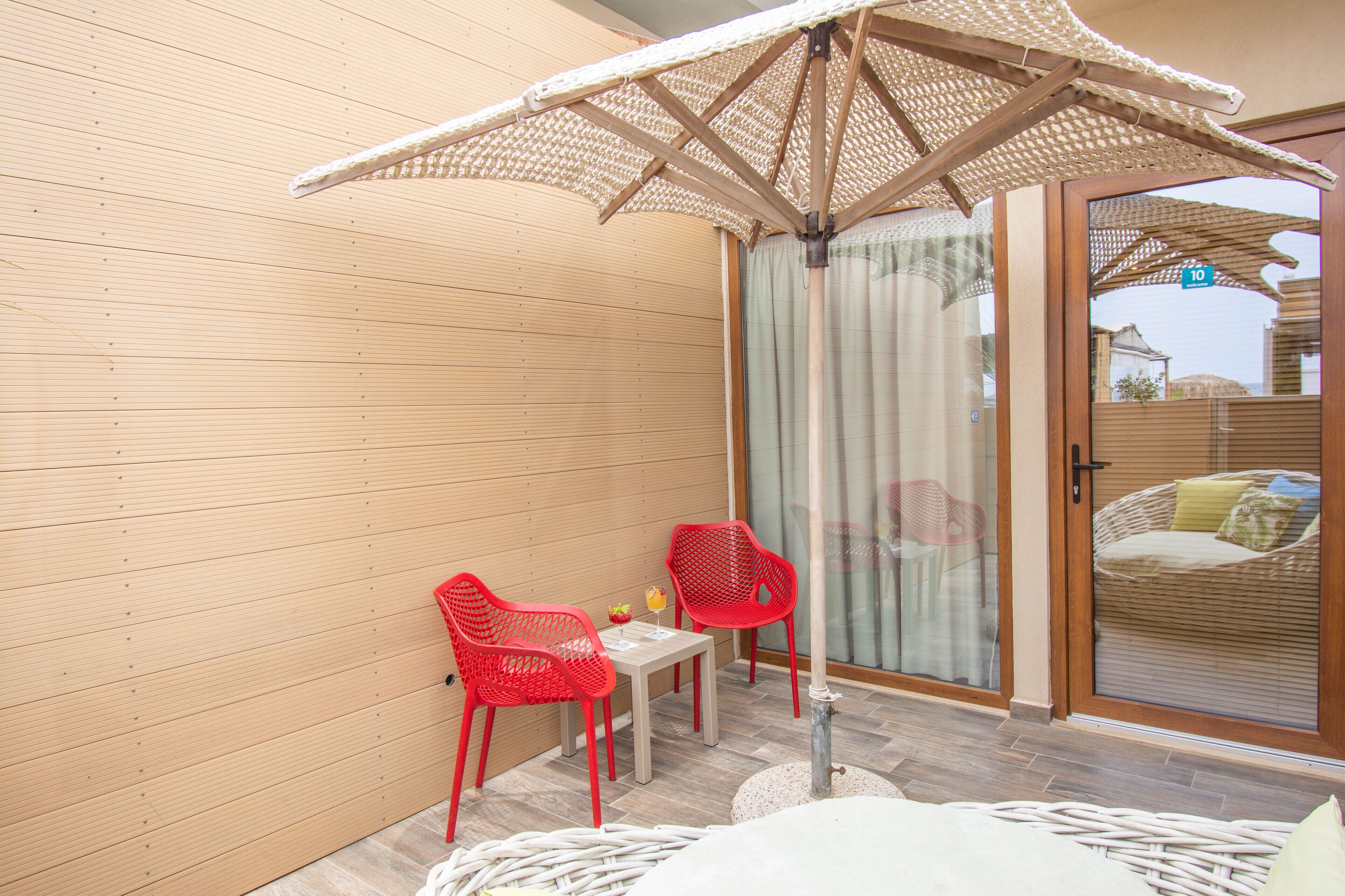 A balcony with a table, two red chairs, a wicker sofa, and a large umbrella.