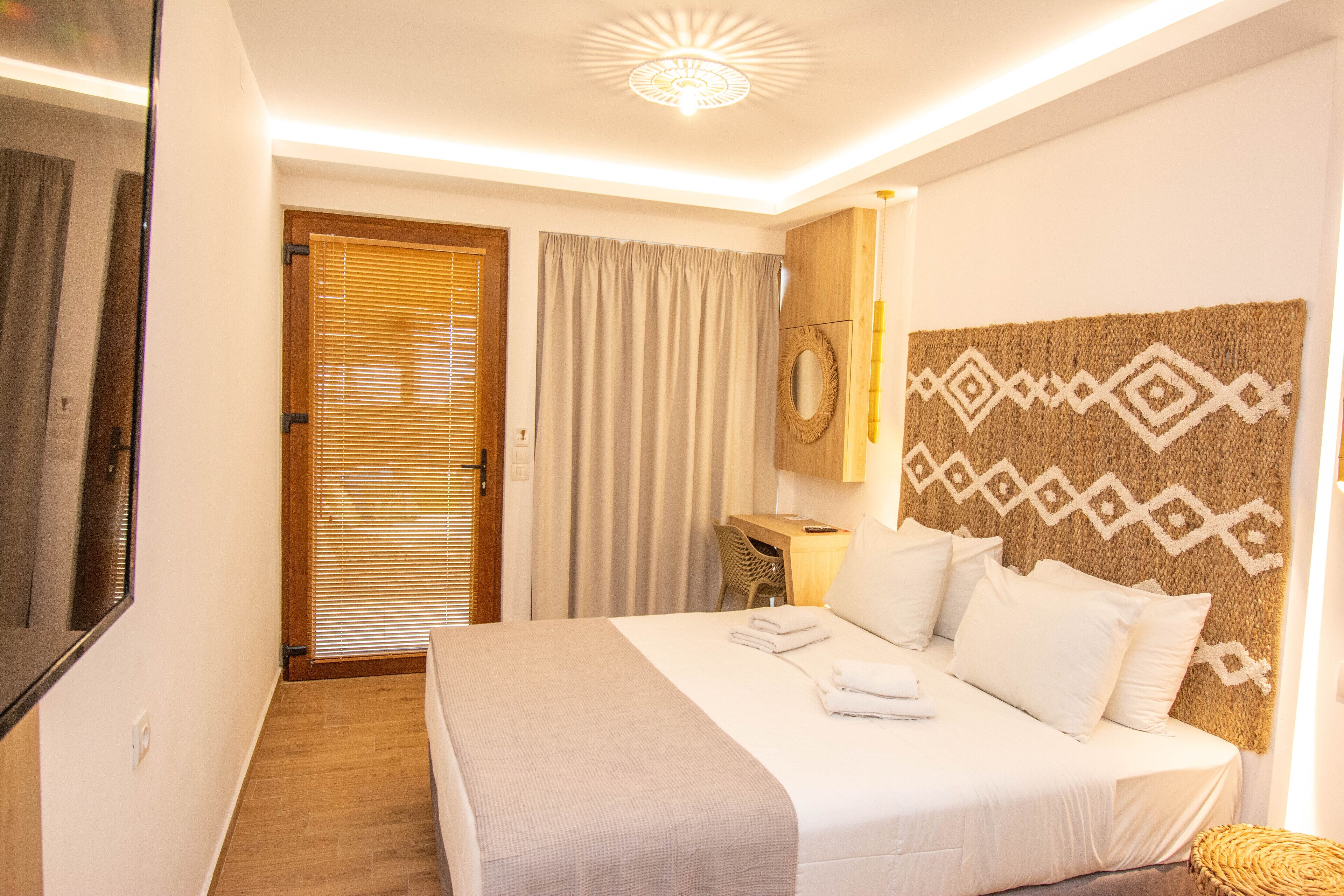 Una habitación de hotel con una cama grande, un escritorio de madera, un espejo y un cabecero estampado.