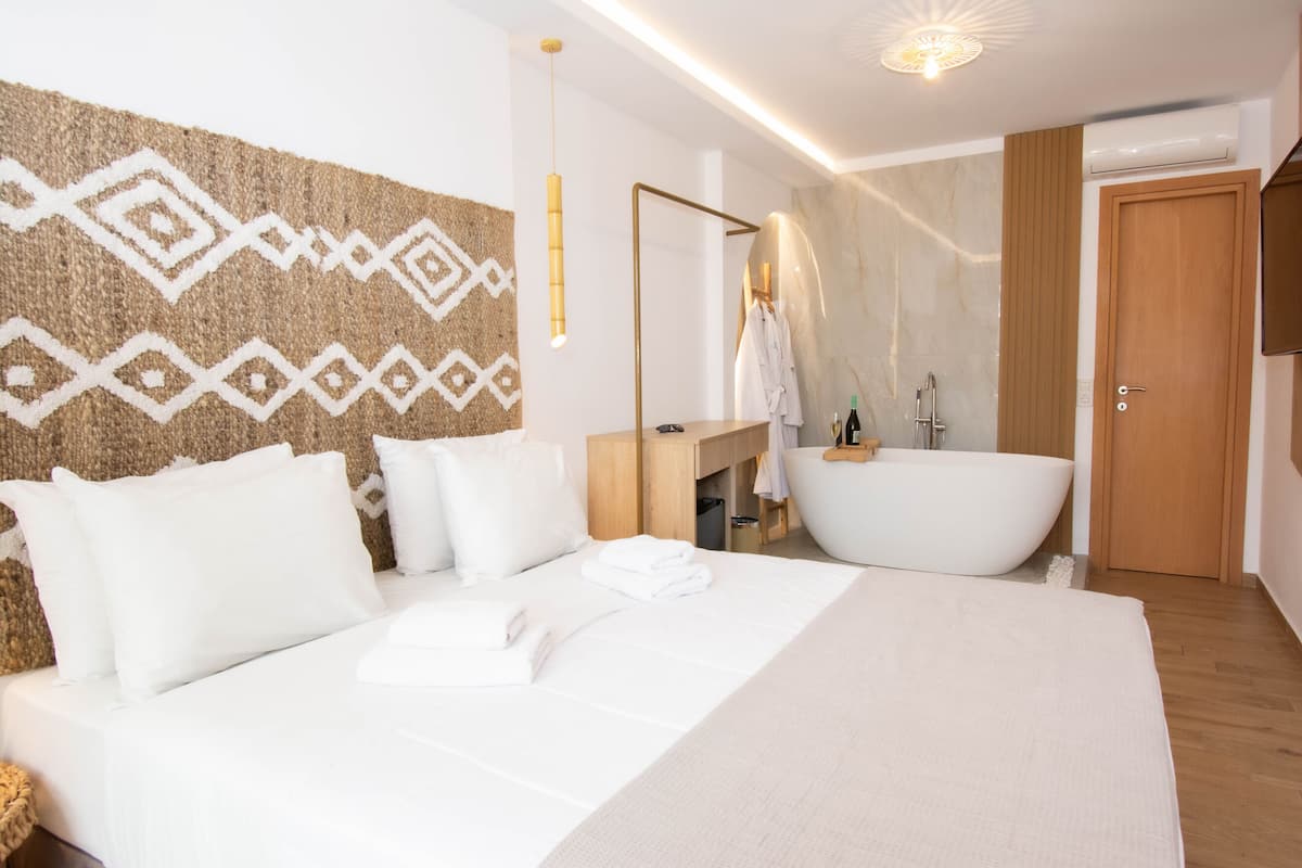 Una habitación de hotel moderna con una cama grande, una bañera, piso de madera y un espejo.