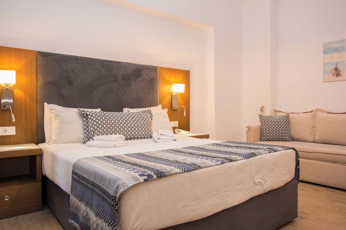 Habitación de hotel con una cama grande, mesitas de noche, un sofá y un cuadro en la pared.