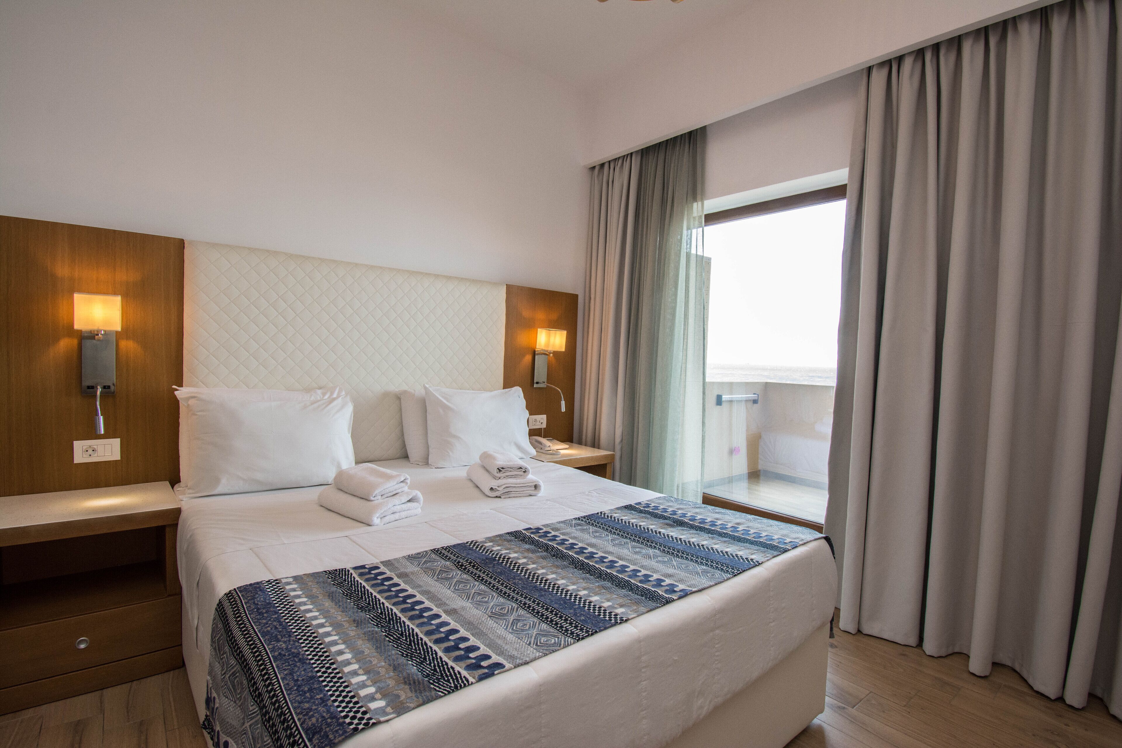 Habitació d'hotel amb un llit gran, dues taules de nit, una finestra amb cortines i vista a l'exterior.