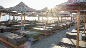 Un espace de détente aménagé sur la plage, avec plusieurs chaises longues et des parasols en chaume.