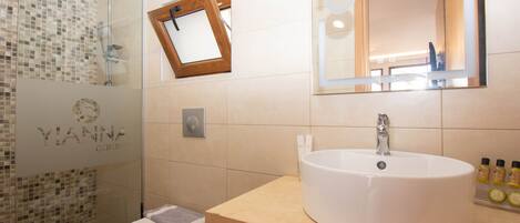 Un baño con cabina de ducha de vidrio, inodoro, lavabo con espejo y artículos de aseo sobre el lavabo.
