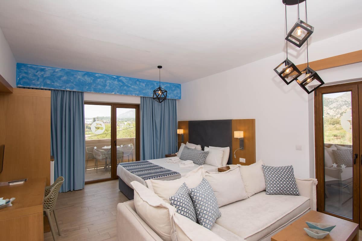 Habitación de hotel con cama, sofá, escritorio y balcón con vistas.