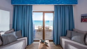 Une pièce avec vue sur la plage, comprenant deux canapés ornés de coussins à motifs, une table basse en bois et une grande fenêtre avec des rideaux bleus.