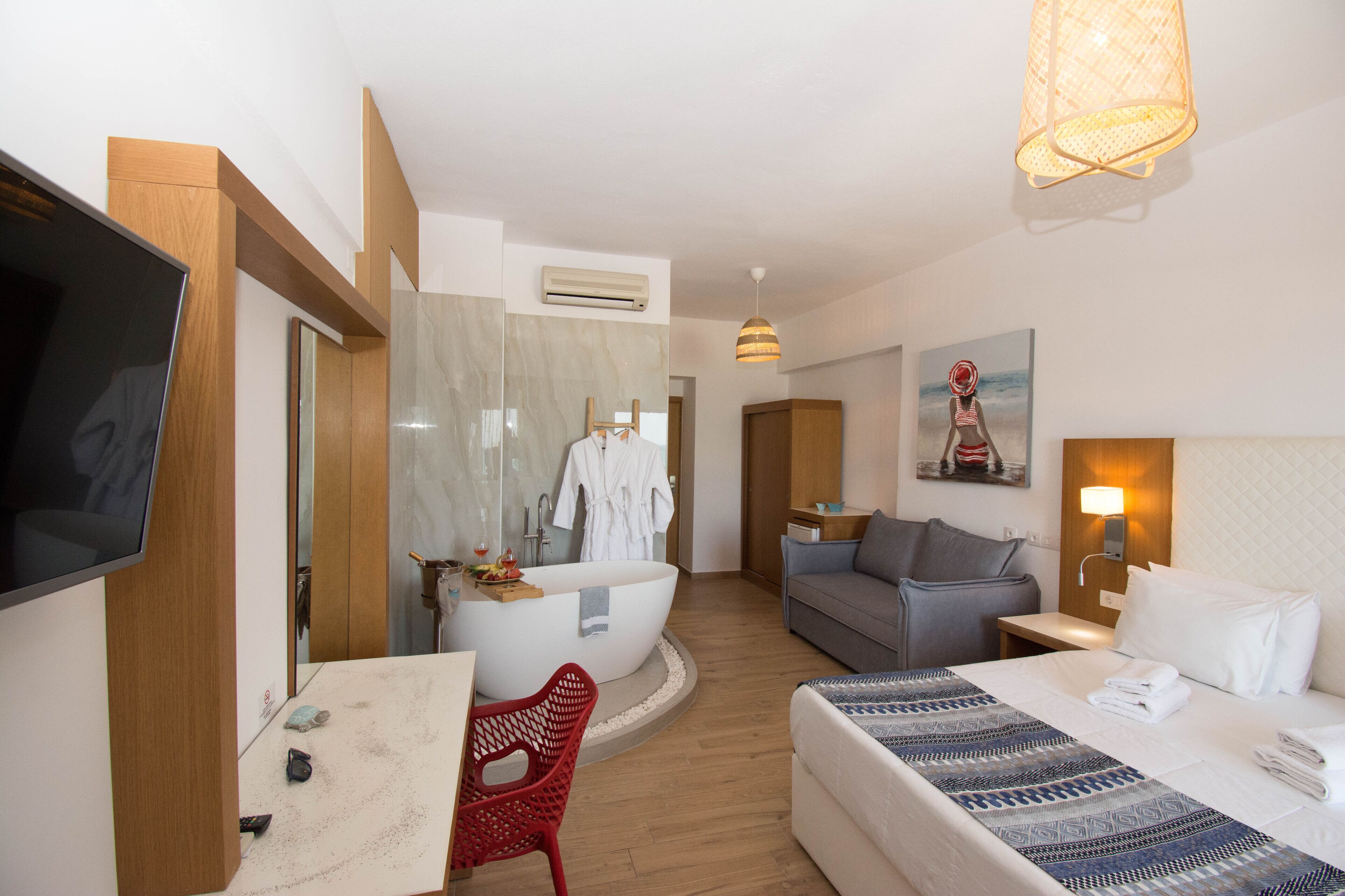 Habitación de hotel con cama, escritorio, televisor y baño con bañera y ducha.