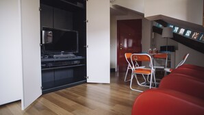 Moderni olohuone, jossa on taulutelevisio, ruokapöytä tuoleineen ja portaikko, joka johtaa ylempään kerrokseen.