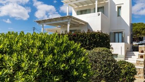 A modern white building with a flat roof, a covered porch, and a stone staircase leading to the entrance. - Maisons a la Plage (Sifnos)