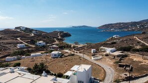 A coastal village with white buildings, a winding road, and a view of the sea and distant hills. - Maisons a la Plage (Sifnos)