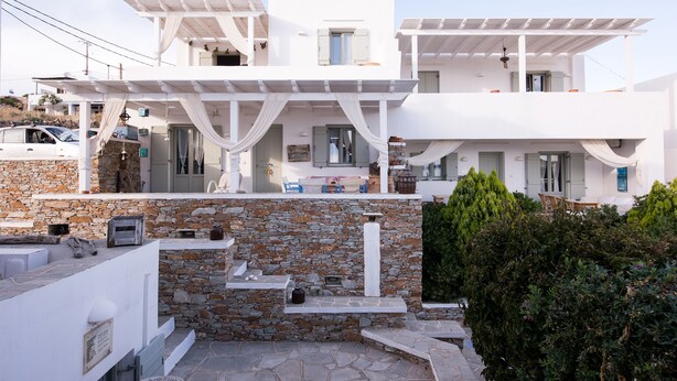 A white building with a stone facade, a covered outdoor seating area, and a stone staircase leading to the entrance. - Maisons a la Plage (Sifnos)