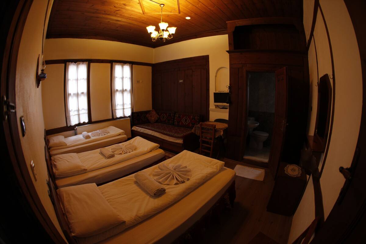 Ein Zimmer mit drei Betten, Holzbalkendecke, einer Bank und einem kleinen Tisch.