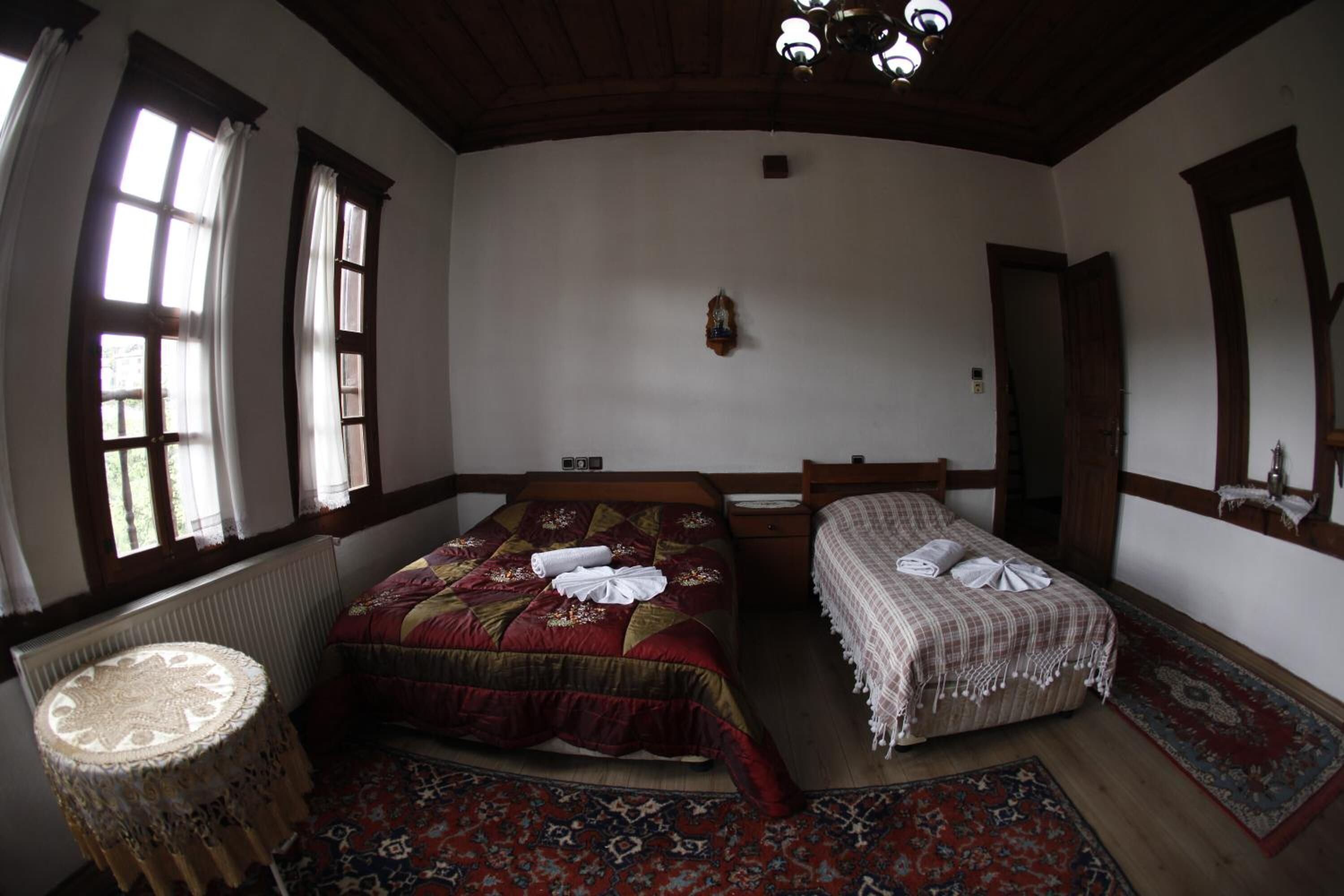 Une chambre traditionnelle avec deux lits, une table ronde et une grande fenêtre avec des rideaux.