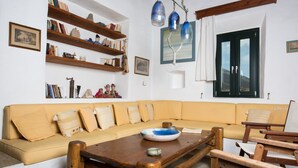 Een woonkamer met een beige bank, een houten salontafel en planken met boeken en decoratieve objecten.