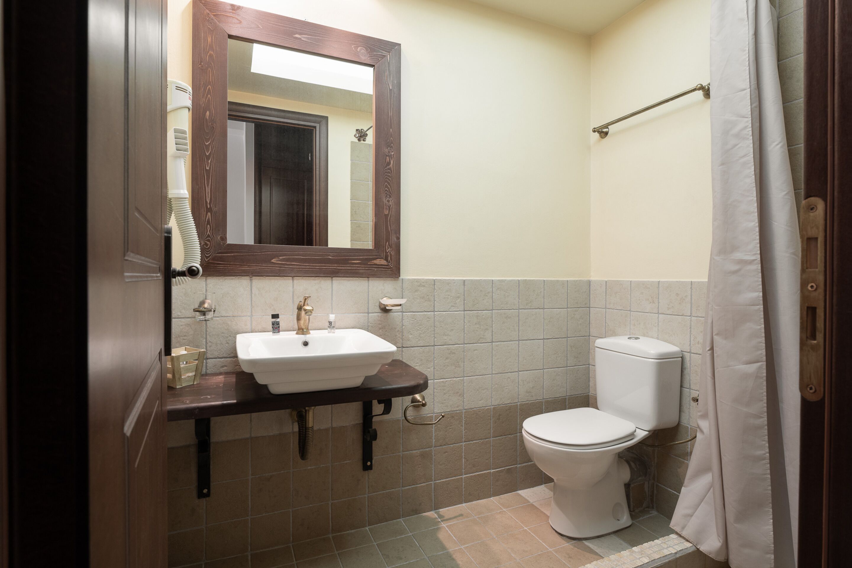 A bathroom with a sink, mirror, toilet, and shower curtain.