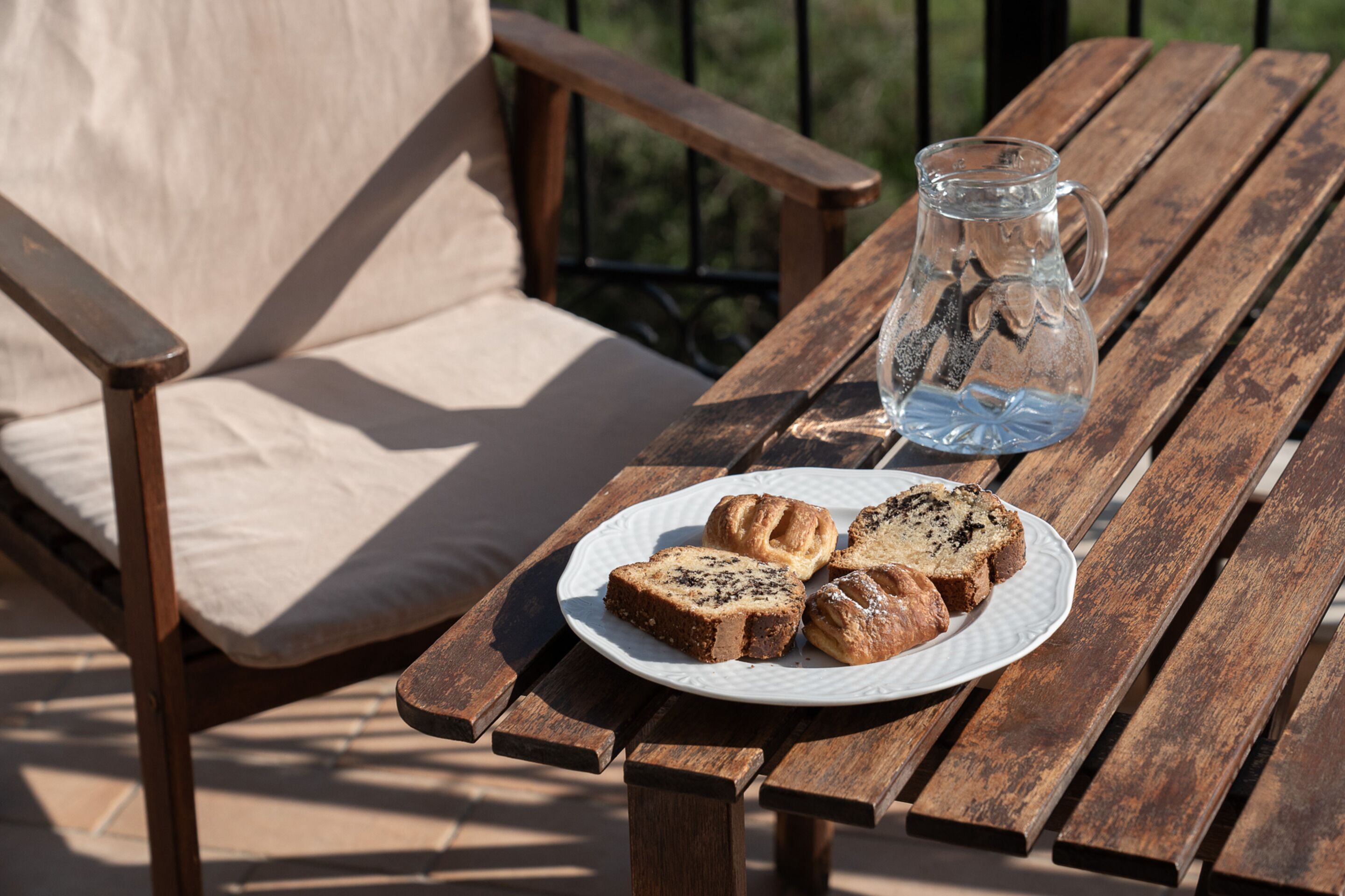 A wooden table with a plate of pastries and a glass pitcher.