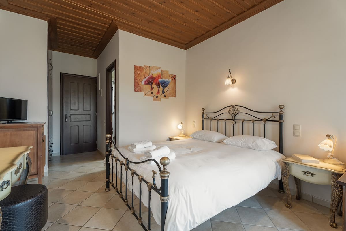 Um quarto com cama, mesas de cabeceira, televisão e um quadro na parede.