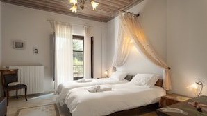 A bedroom with two beds, a chair, a table, and a window with curtains. - Xenonas Ouranogiton (South Kynouria)